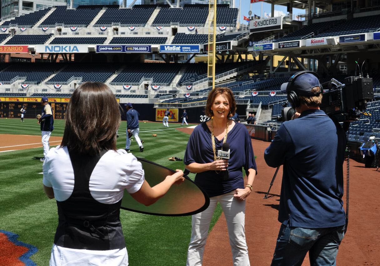 Jane stands on the field at Petco Park. A video crew is filming her for a segment for her show.